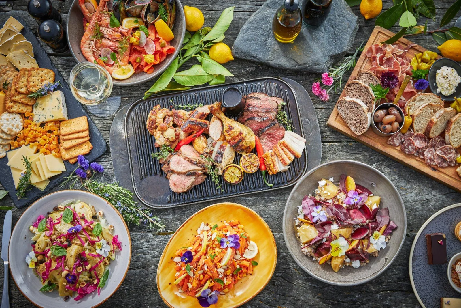 The Walter Peak BBQ buffet laid out — grilled local meats on a cast-iron plate surrounded by salads, charcuterie boards, breads and seafood