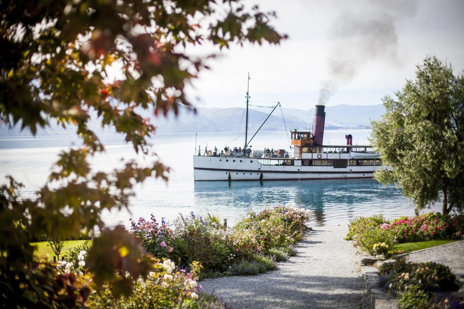 The TSS Earnslaw berthed at Walter Peak, framed by autumn foliage and the homestead's lakeside flower beds