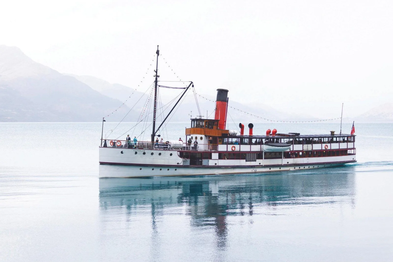 The TSS Earnslaw under steam on a still Lake Whakatipu, mountains fading into mist behind her