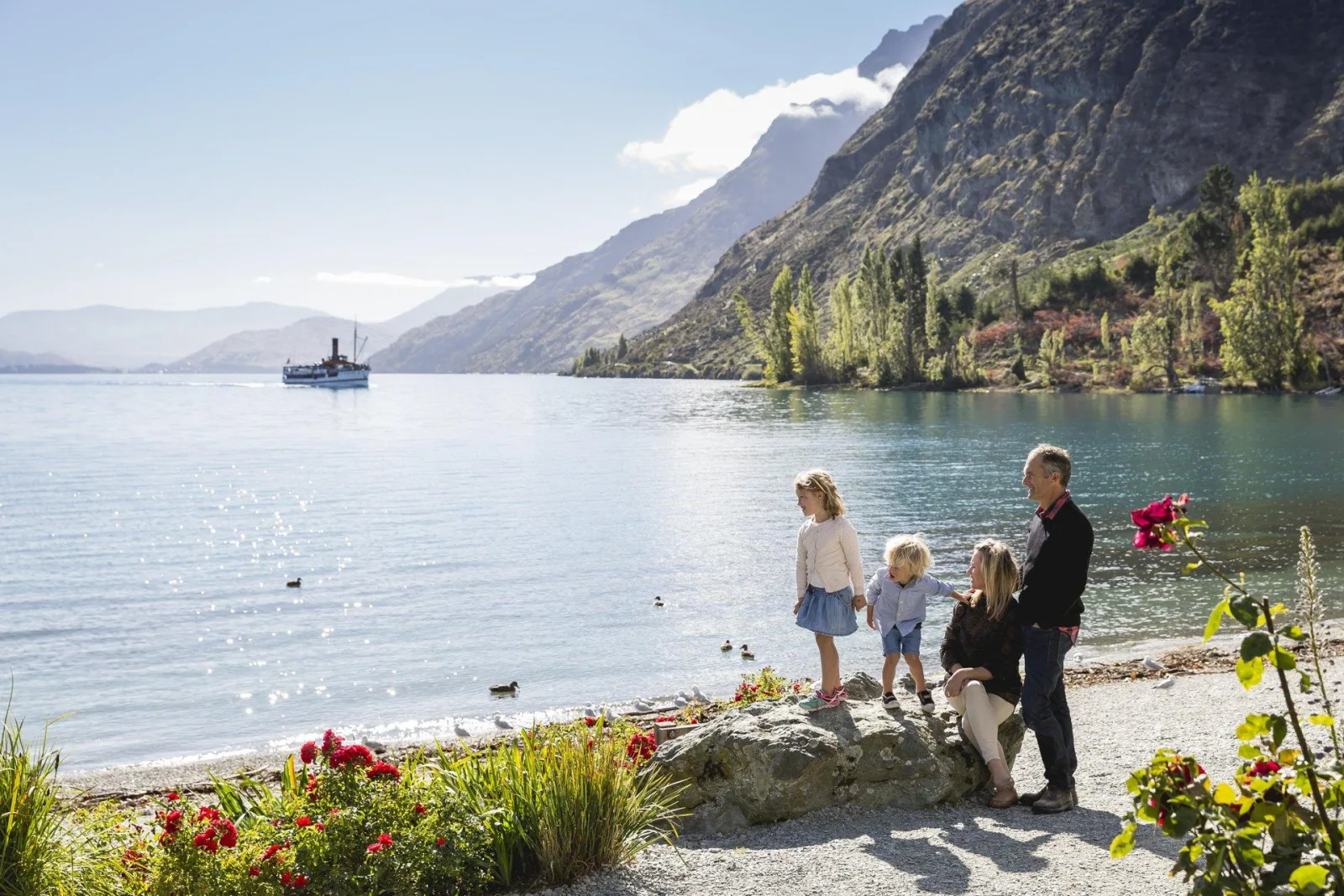 A family standing on the Walter Peak foreshore watching the steamship approach across the lake