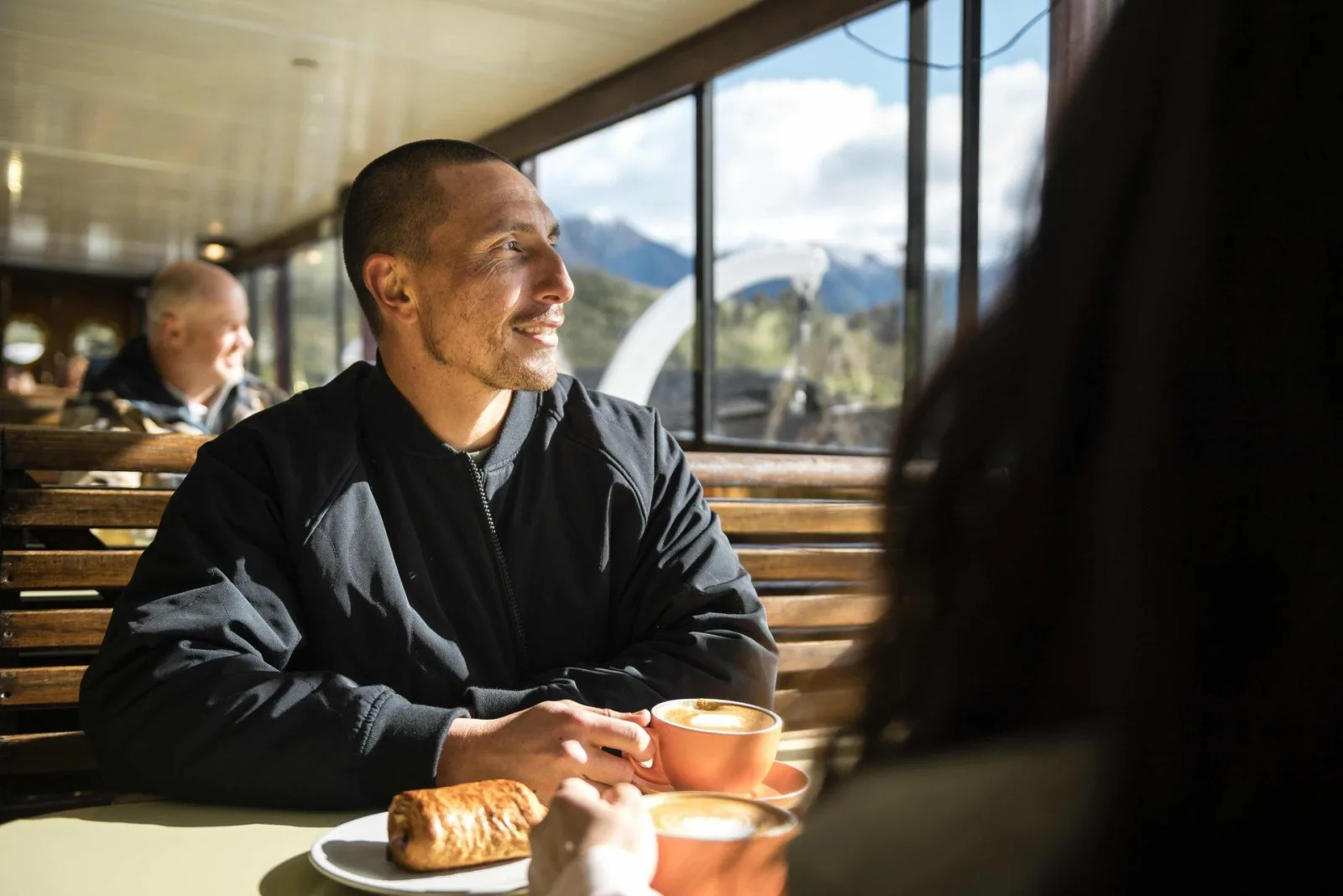 A passenger with coffee and a pastry at a varnished window table in the TSS Earnslaw saloon