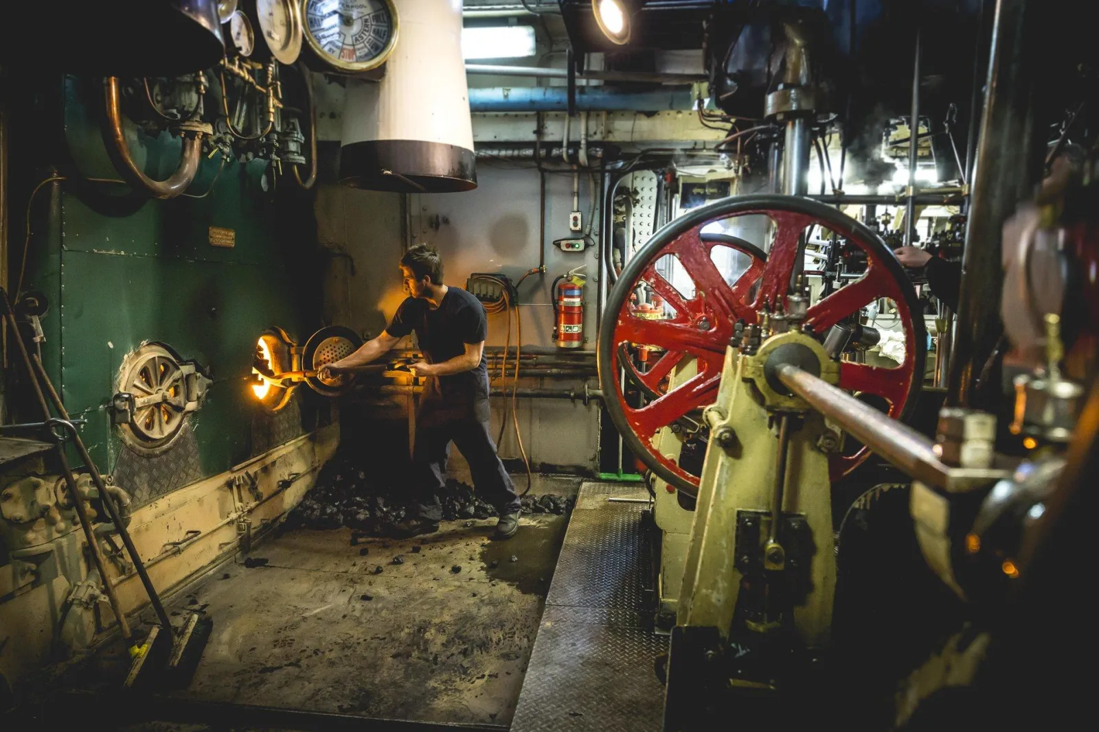 A stoker shovelling coal into the glowing fireboxes in the TSS Earnslaw's engine room