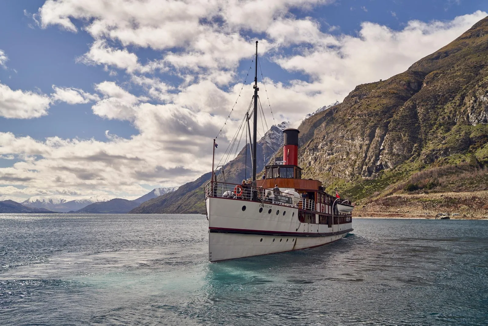 The TSS Earnslaw under a plume of steam on Lake Whakatipu with a sheer mountain wall behind
