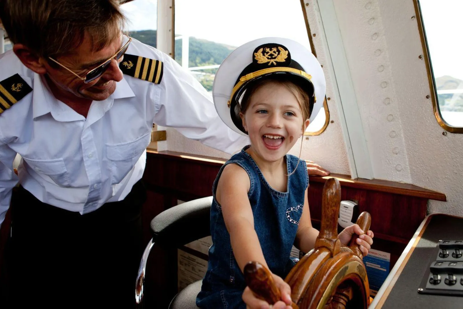 The skipper letting a child hold the wheel in the wheelhouse of the Million Dollar Cruise boat