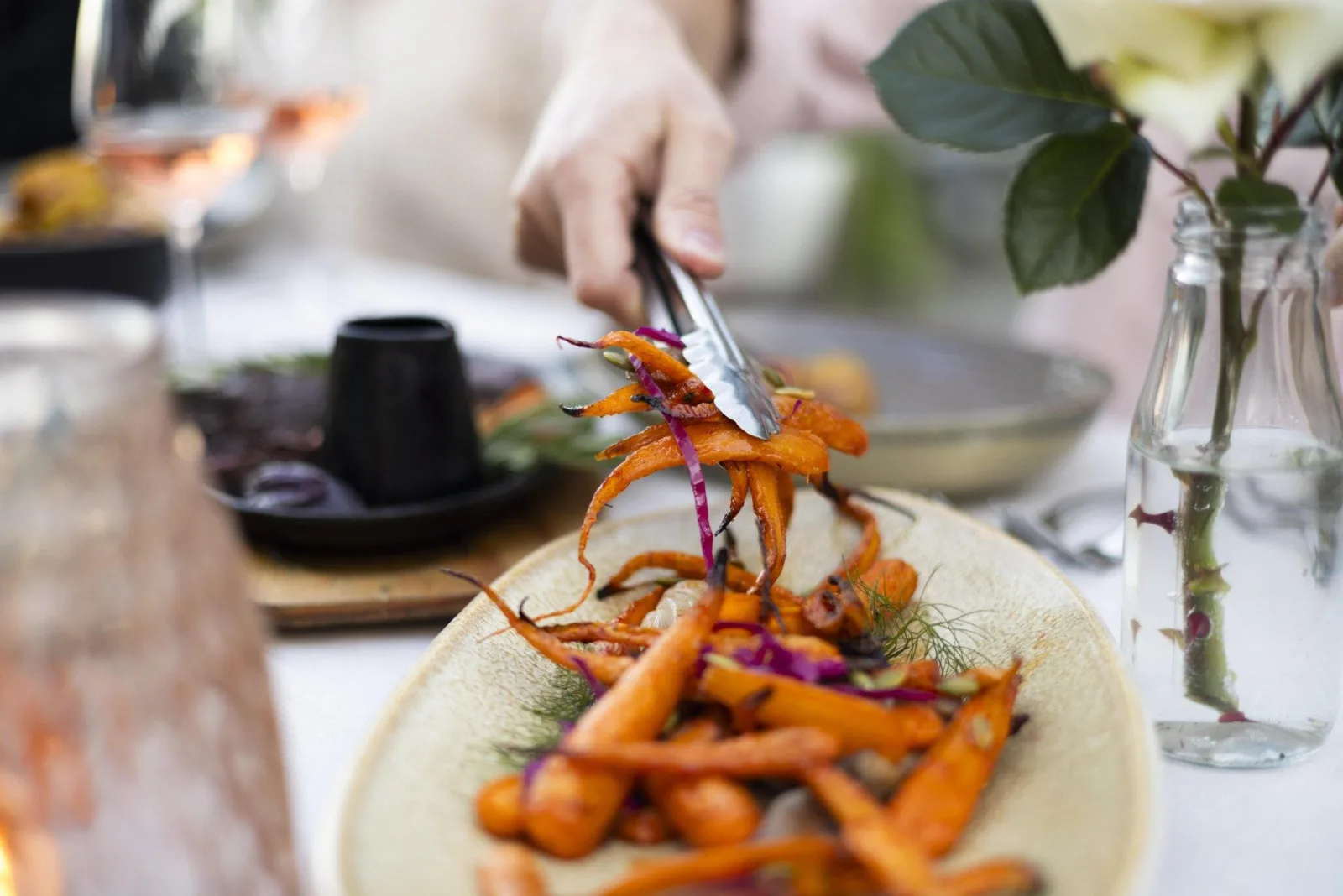 Roast carrots being lifted onto a plate at the buffet, with flowers and condiments on the table behind